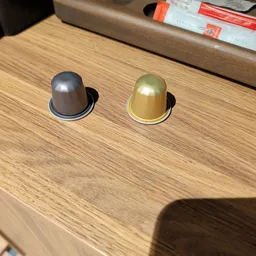 Twee koffiecapsules in verschillende kleuren (grijs en goud) op houten tafel