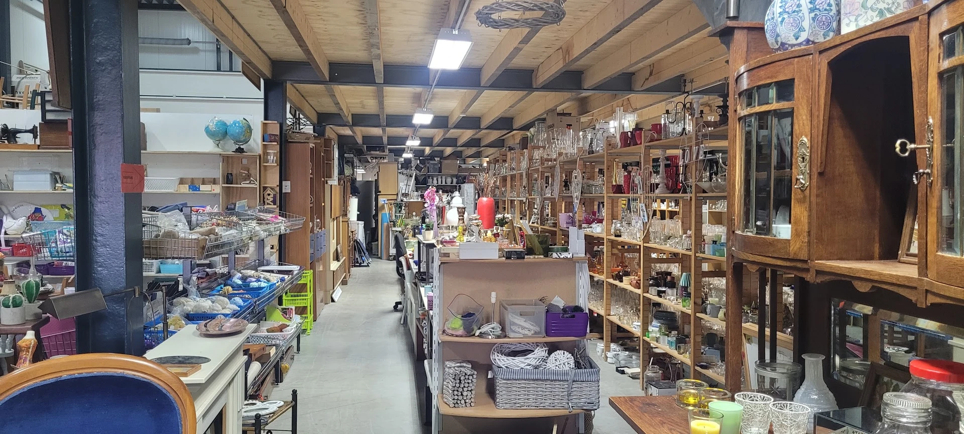 Overzicht van de winkelvloer met houten stellingen vol huishoudartikelen en diverse gebruiksgoederen