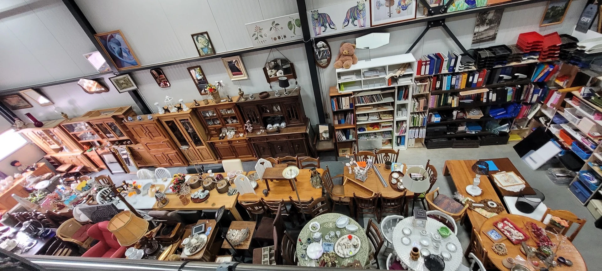 Overzicht van kringloopwinkel met boeken, servies, meubels en decoratieve items uitgestald op tafels en in kasten