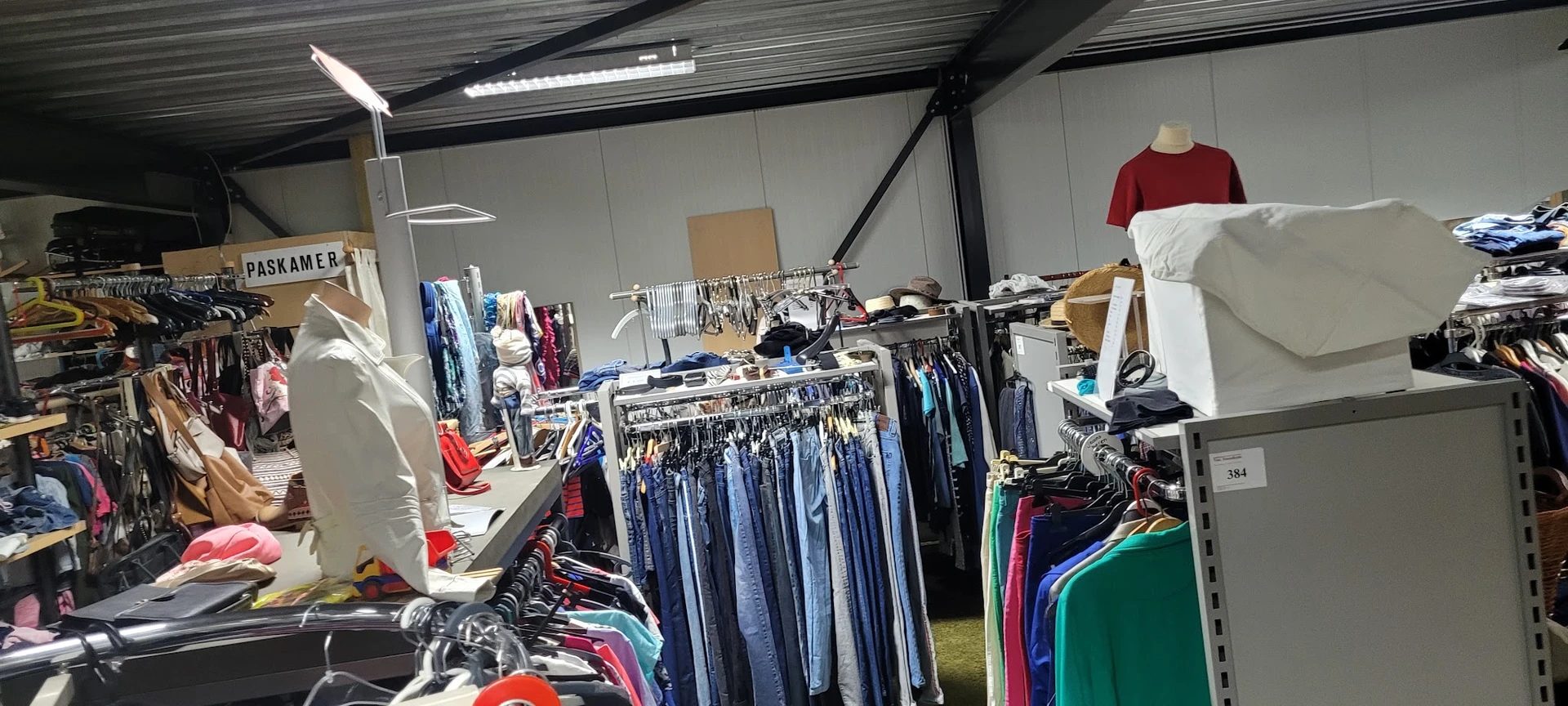 Rekken met tweedehands kleding, vooral jeans en donkerblauwe items, in een kringloopwinkel