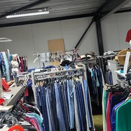 Rekken met tweedehands kleding, vooral jeans en donkerblauwe items, in een kringloopwinkel