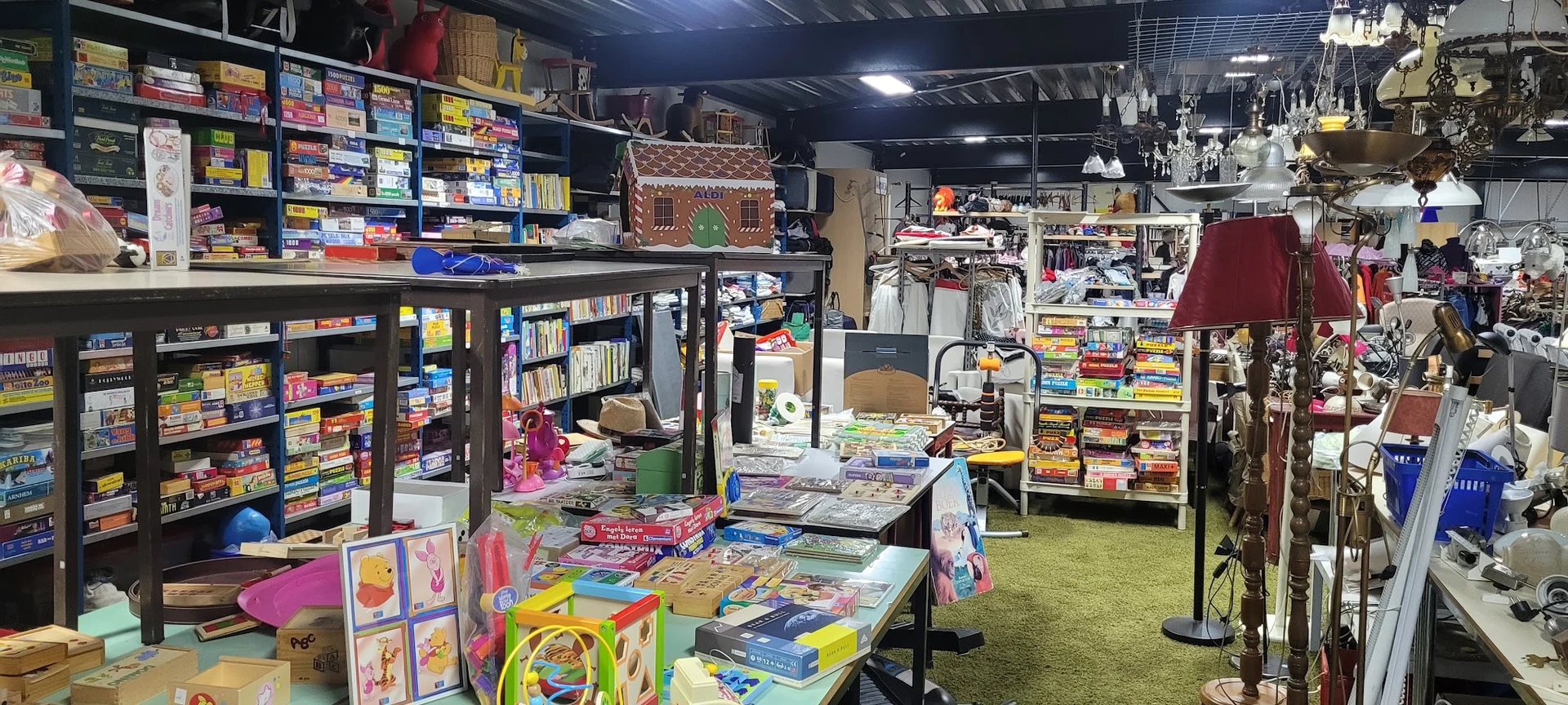 Winkelvloer met speelgoed, boeken en kinderspullen op tafels en stellingen, groene vloerbedekking