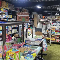 Winkelvloer met speelgoed, boeken en kinderspullen op tafels en stellingen, groene vloerbedekking