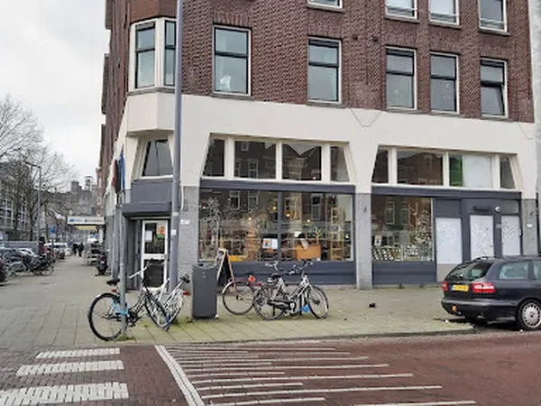 Gevel van kringloopwinkel aan straathoek met witte pui, grote ramen en fietsen ervoor