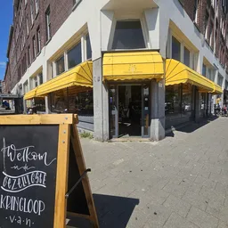 Winkelhoek met gele luifels en zwarte pui aan straat met terras