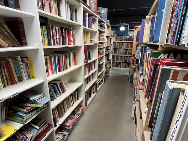 Gangpad tussen witte boekenkasten vol met dvd's, blu-rays en boeken in een kringloopwinkel