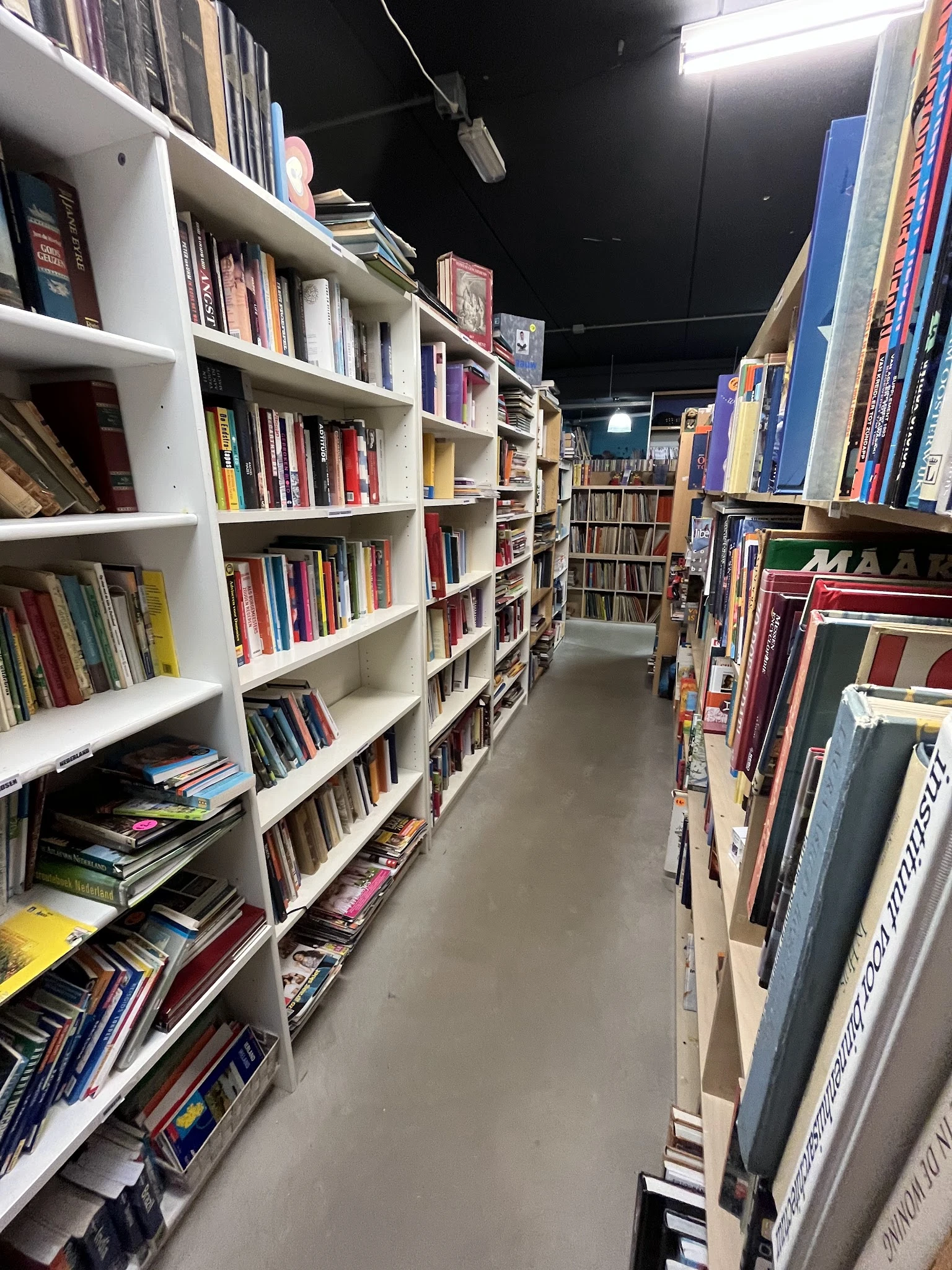 Gangpad tussen witte boekenkasten vol met dvd's, blu-rays en boeken in een kringloopwinkel