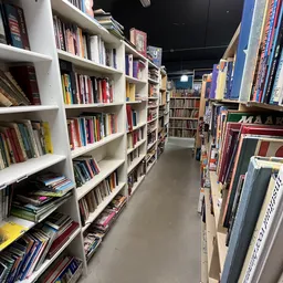 Gangpad tussen witte boekenkasten vol met dvd's, blu-rays en boeken in een kringloopwinkel