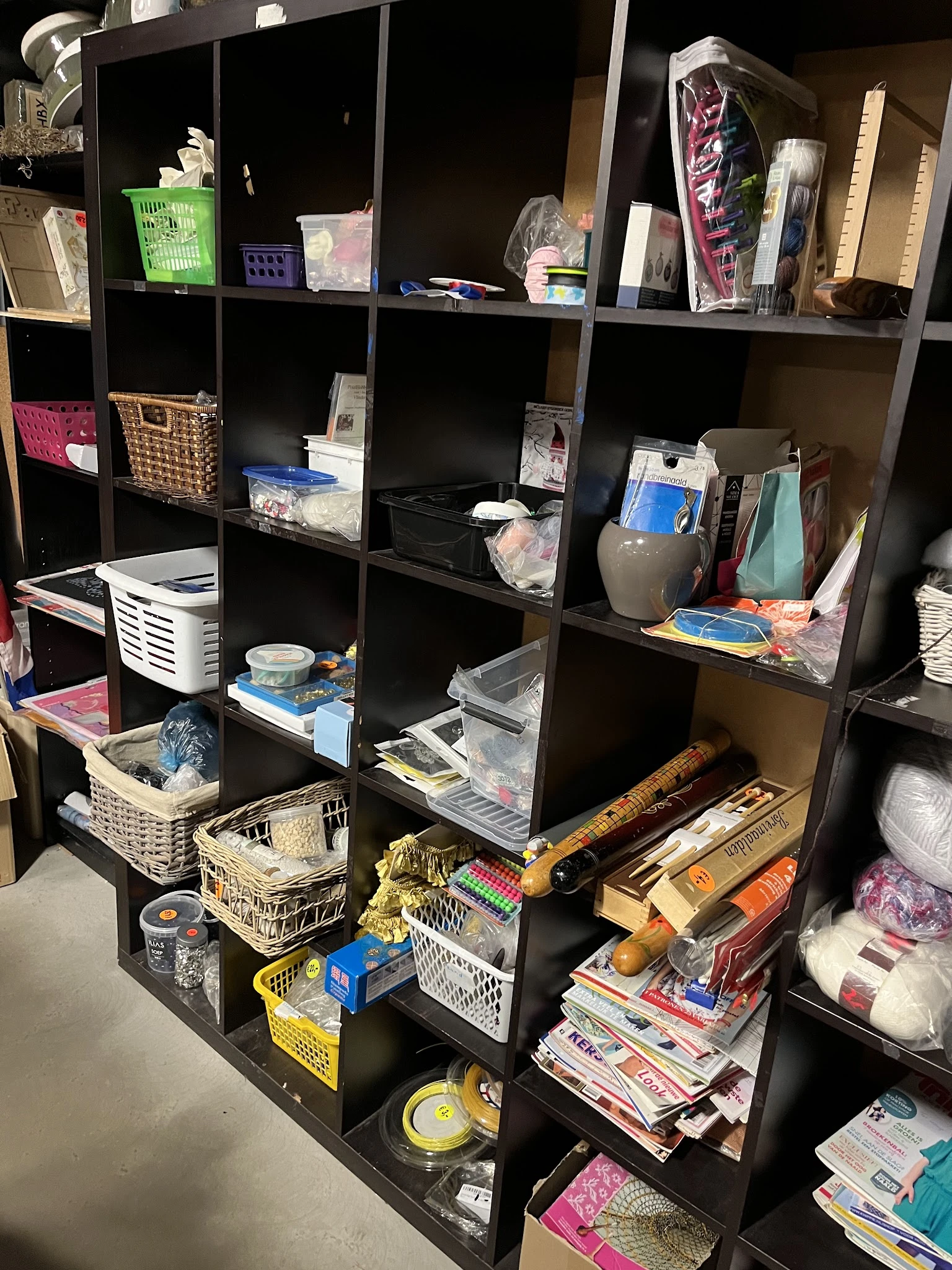 Stellingkast met verschillende huishoudelijke artikelen, keukengereedschap en opbergmanden in een kringloopwinkel