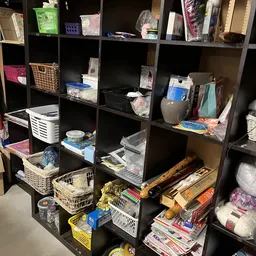 Stellingkast met verschillende huishoudelijke artikelen, keukengereedschap en opbergmanden in een kringloopwinkel