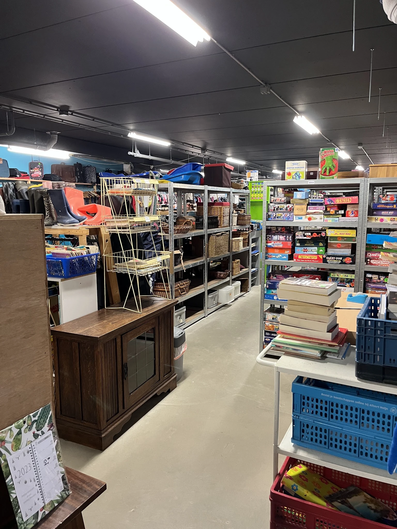 Winkelvloer met stellingen vol boeken, spellen en huishoudartikelen, met een houten meubel op de voorgrond