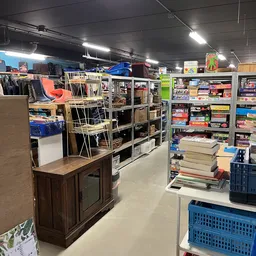 Winkelvloer met stellingen vol boeken, spellen en huishoudartikelen, met een houten meubel op de voorgrond