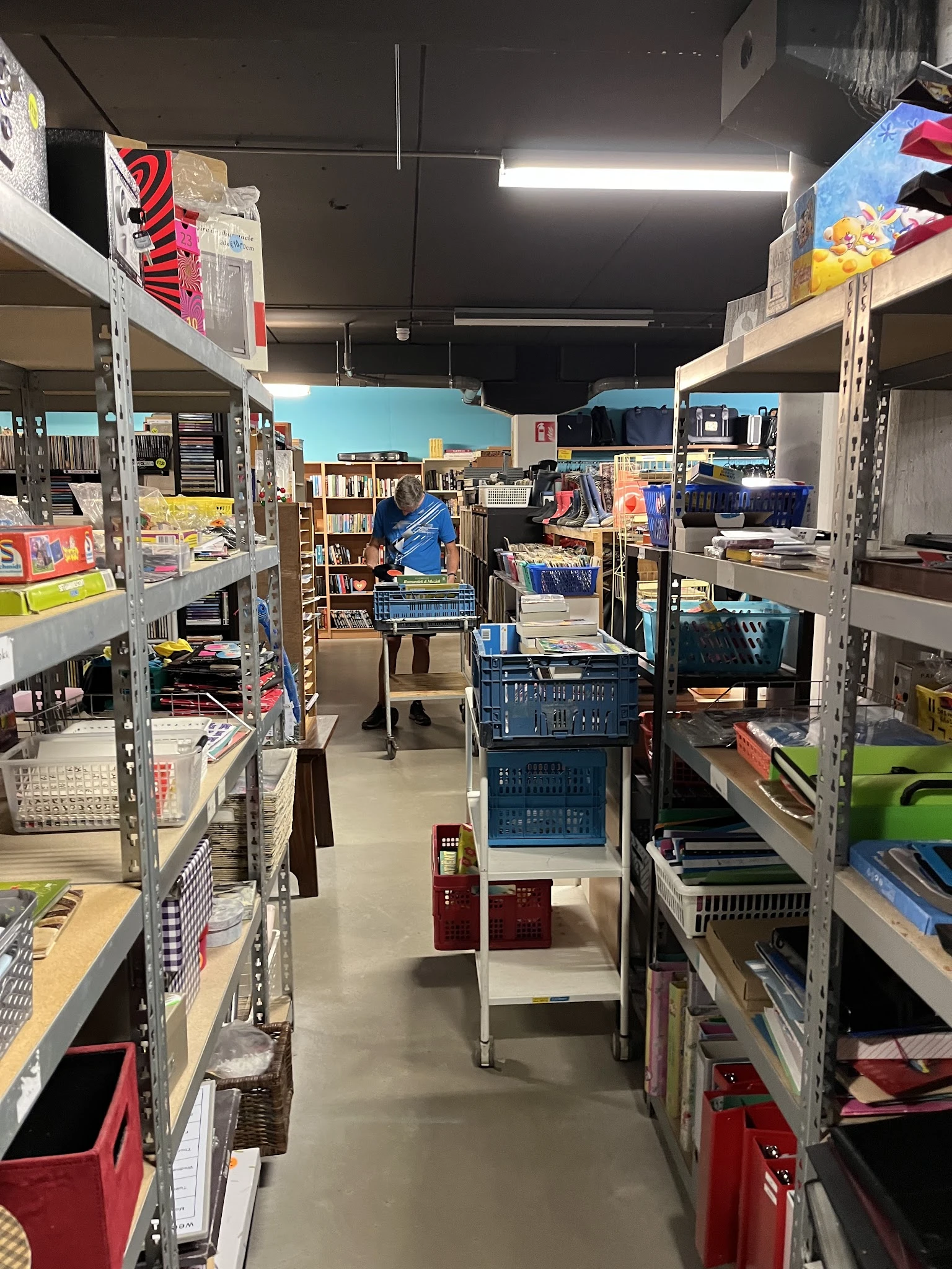 Winkelvloer met metalen stellingen vol boeken, kleding en huishoudartikelen, blauw winkelwagen in het midden