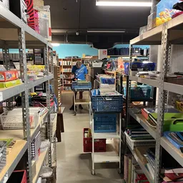 Winkelvloer met metalen stellingen vol boeken, kleding en huishoudartikelen, blauw winkelwagen in het midden