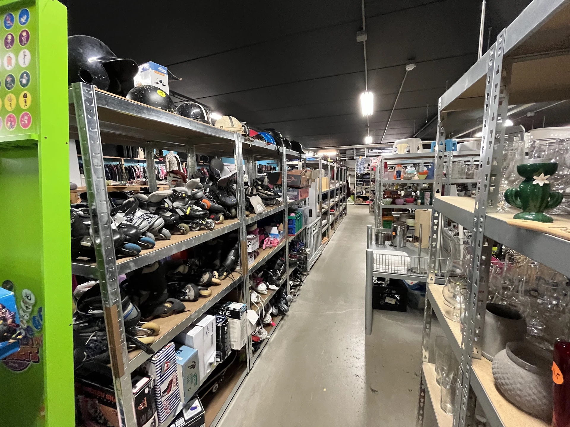 Winkelinterieur met metalen stellingen vol tweedehands artikelen, schoenen en kleding onder heldere verlichting
