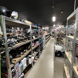 Winkelinterieur met metalen stellingen vol tweedehands artikelen, schoenen en kleding onder heldere verlichting