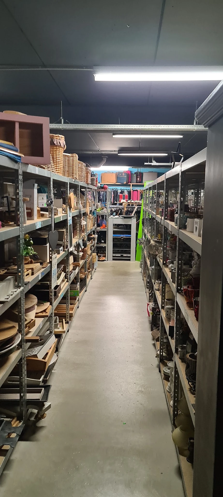 Gangpad tussen stellingen met huishoudelijke artikelen, kleding en diverse spullen in een kringloopwinkel