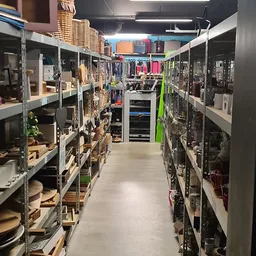 Gangpad tussen stellingen met huishoudelijke artikelen, kleding en diverse spullen in een kringloopwinkel