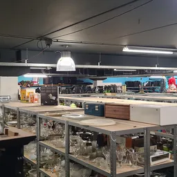Winkelvloer met werkbanken, stellingen vol met spullen en hangende lampen
