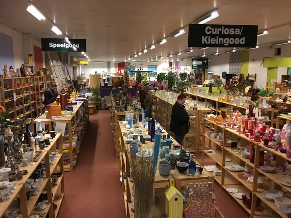 Winkelvloer met houten stellingen vol spullen, twee secties met bordjes 'Speelgoed' en 'Curiosa/Kleingoed', LED-verlichting a