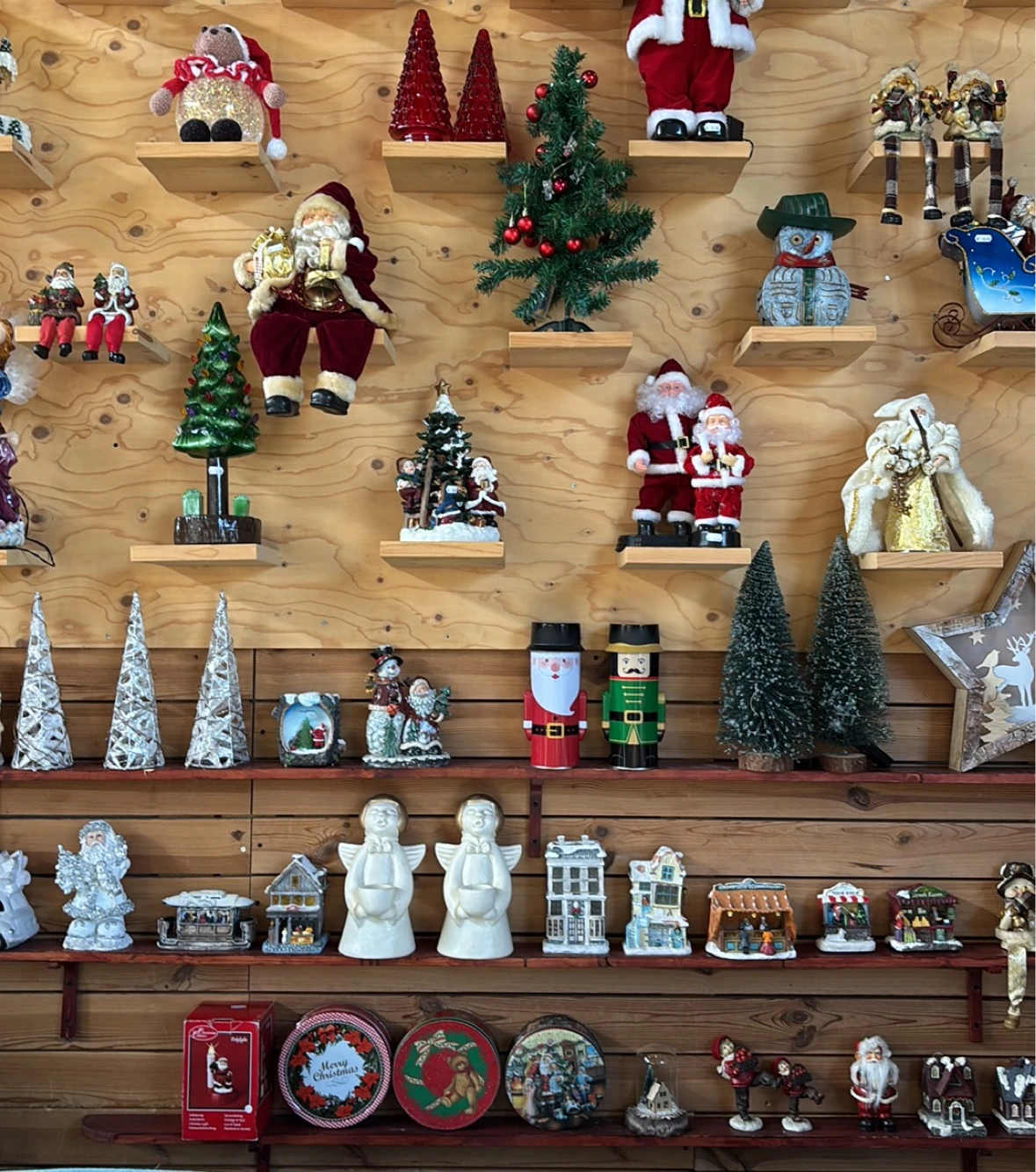 Uitgestalde kerstdecoraties op houten wandrekken: kerstmannen, kerstbomen, sneeuwpoppen en huisjes