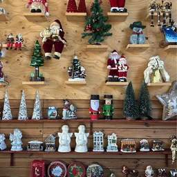 Uitgestalde kerstdecoraties op houten wandrekken: kerstmannen, kerstbomen, sneeuwpoppen en huisjes