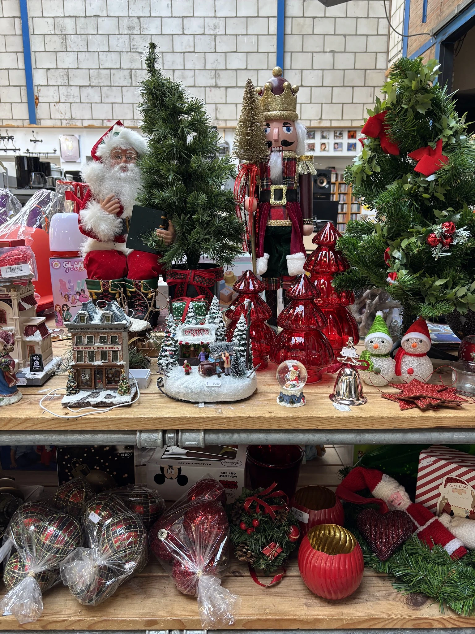 Kerstdecoraties uitgestald op houten toonbank: kerstmanfiguur, sneeuwpoppen, rode versieringen, kersttaferelen en groene denn