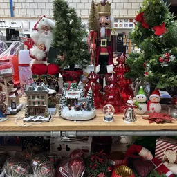 Kerstdecoraties uitgestald op houten toonbank: kerstmanfiguur, sneeuwpoppen, rode versieringen, kersttaferelen en groene denn