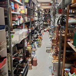 Smalle gangpas tussen stellingen vol spullen in kringloopwinkel, veel rommel op de vloer