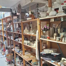 Houten stellingen volgestapeld met huishoudartikelen, servies, lampen en decoratieve voorwerpen in een kringloopwinkel