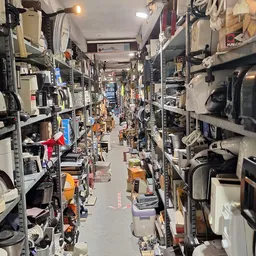Overzicht van de winkelgang tussen stellingen vol elektrotechnische apparaten en huishoudelijke artikelen