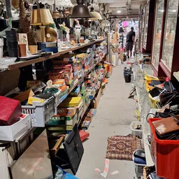 Winkelgangtje met stellingen vol dozen en spullen, zicht op het aanbod in de kringloopwinkel
