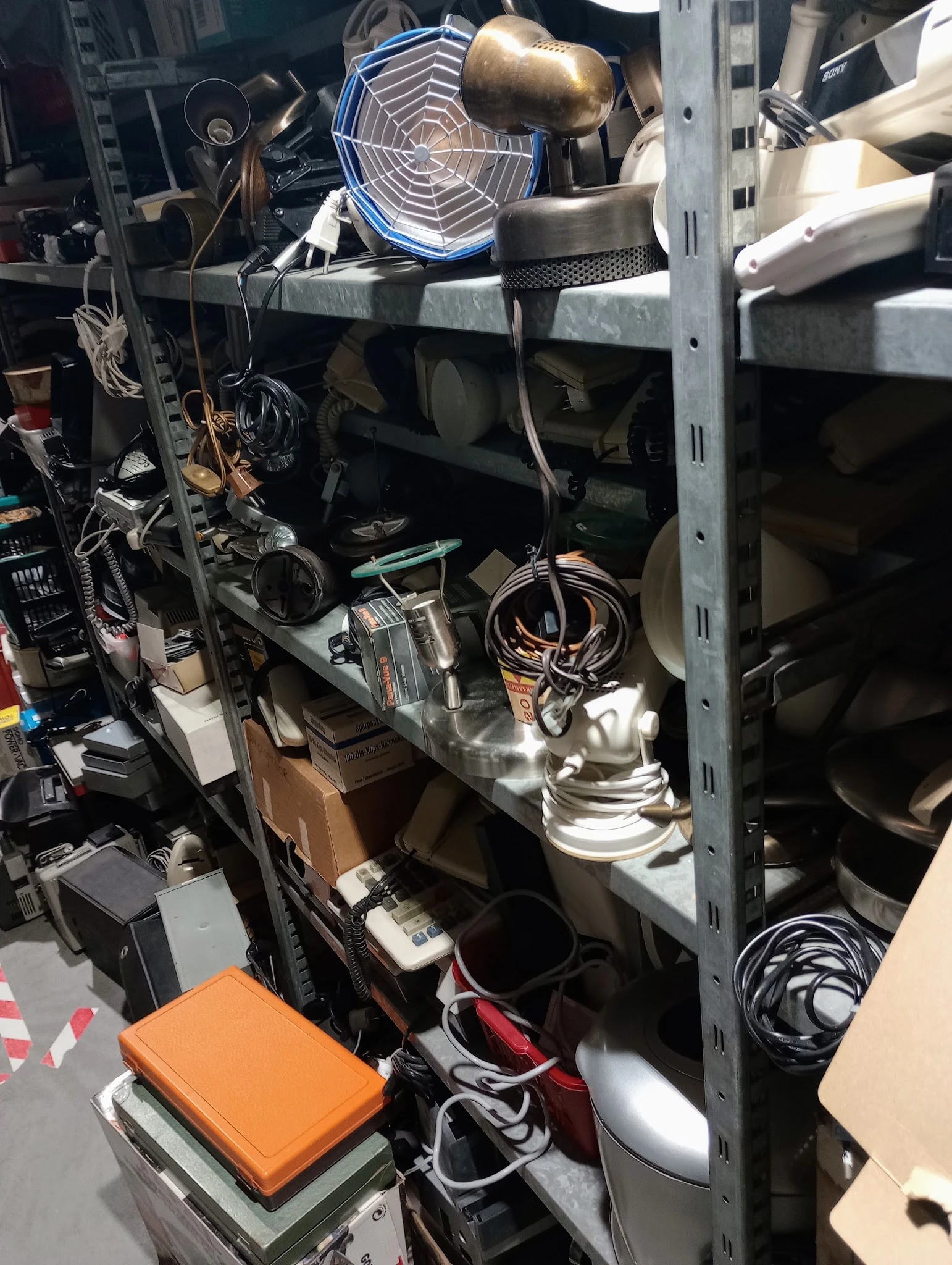Metalen stellingkast met diverse elektrische apparaten en onderdelen zoals lampen en kabels