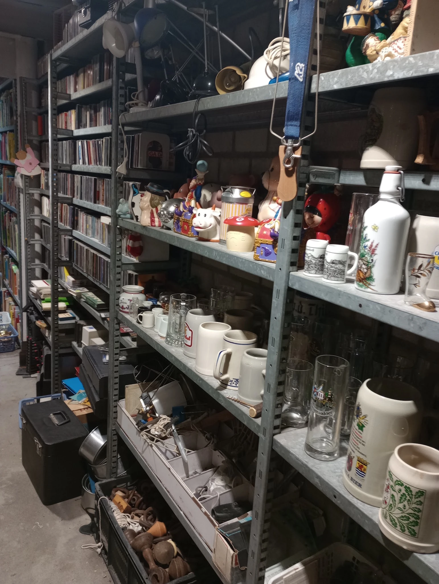 Metalen stellingen met huishoudartikelen zoals bekers, glazen, schalen en decoratieve items in een kringloopwinkel