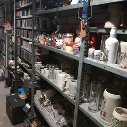 Metalen stellingen met huishoudartikelen zoals bekers, glazen, schalen en decoratieve items in een kringloopwinkel