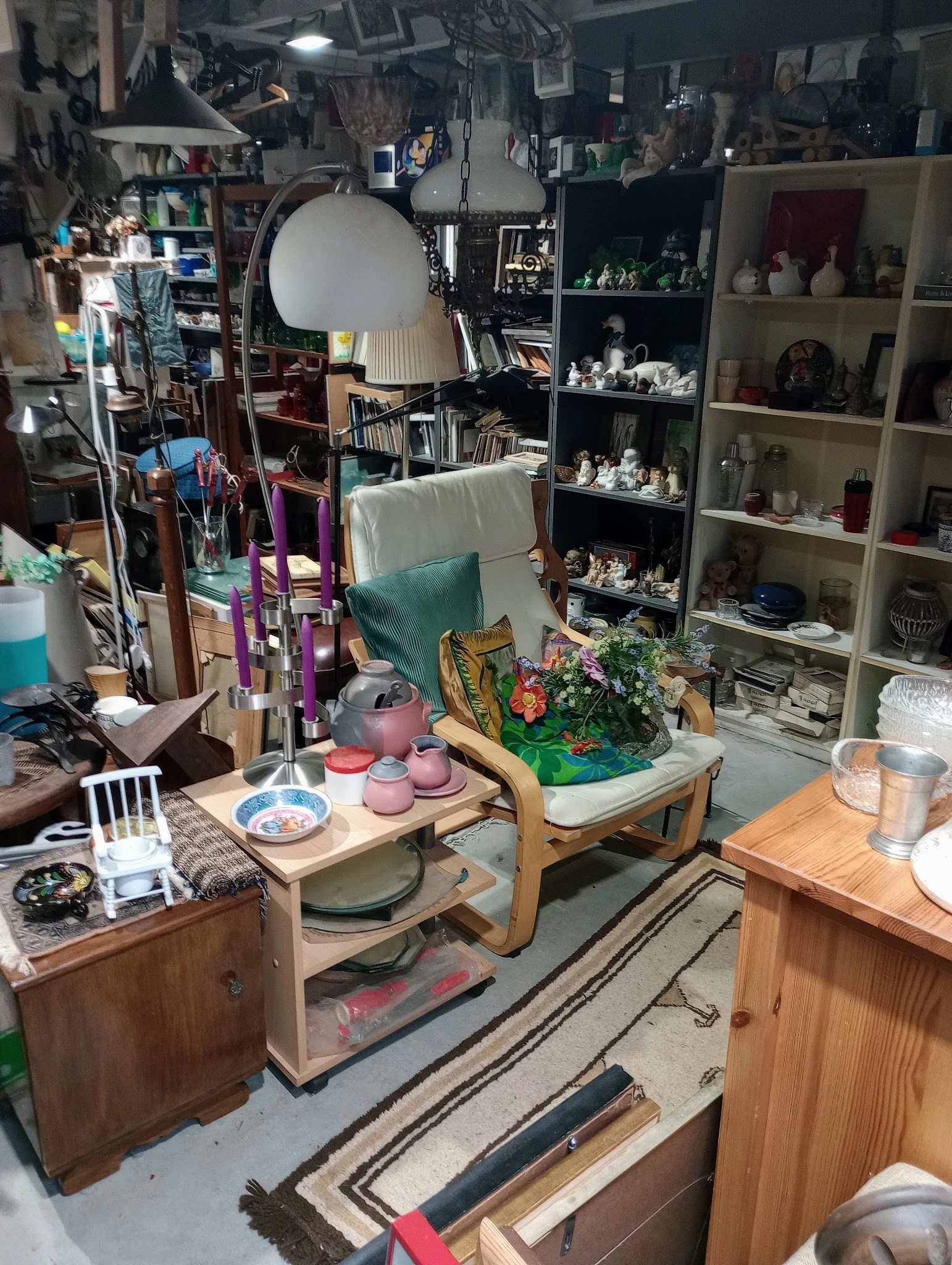 Winkelbinnenruimte met houten tafels, plantenbak, servies, lampen en gevulde stellingen tegen de muur