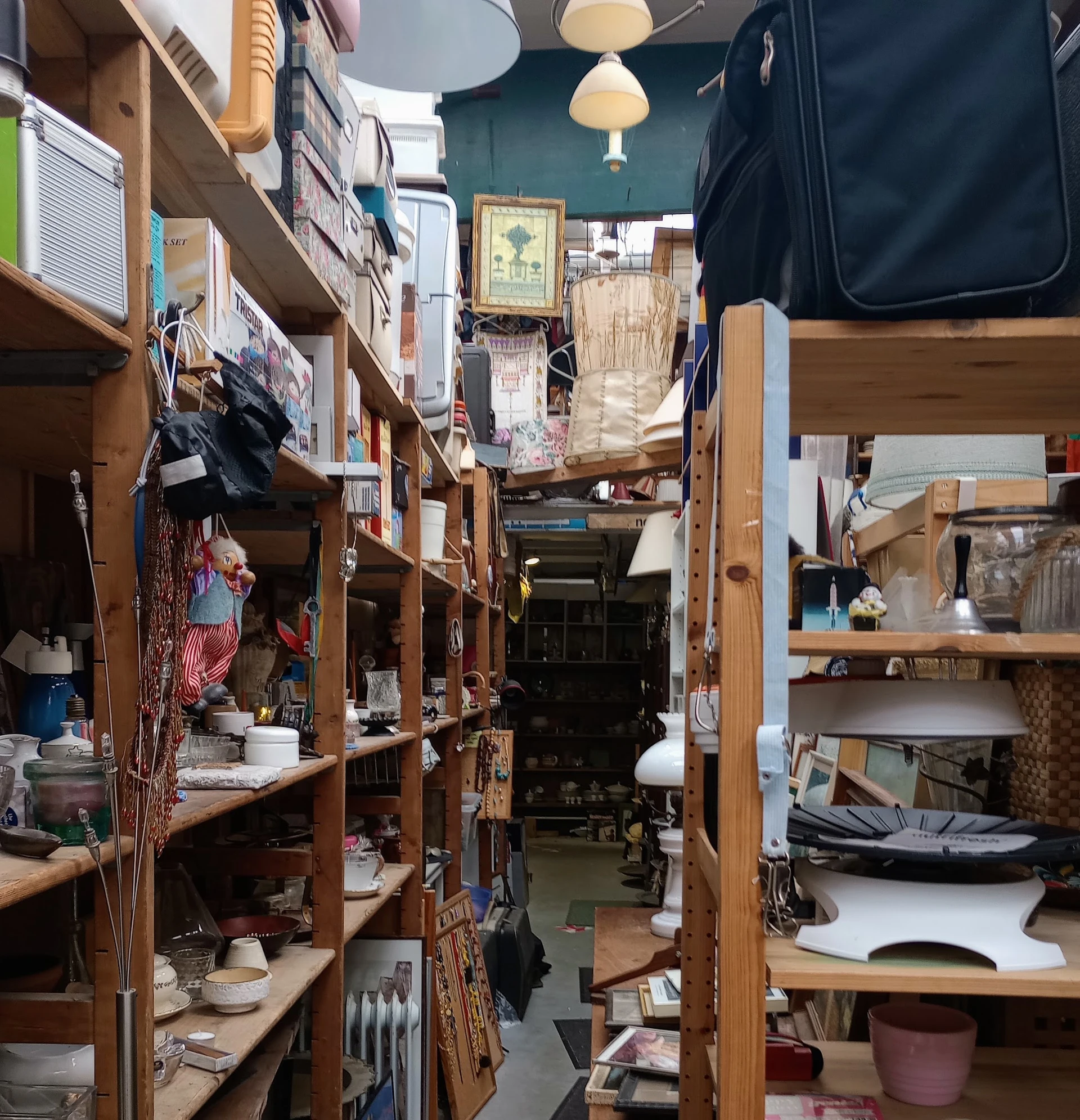 Nauwe gangpad tussen houten stellingen vol tweedehands spullen en kleding in kringloopwinkel