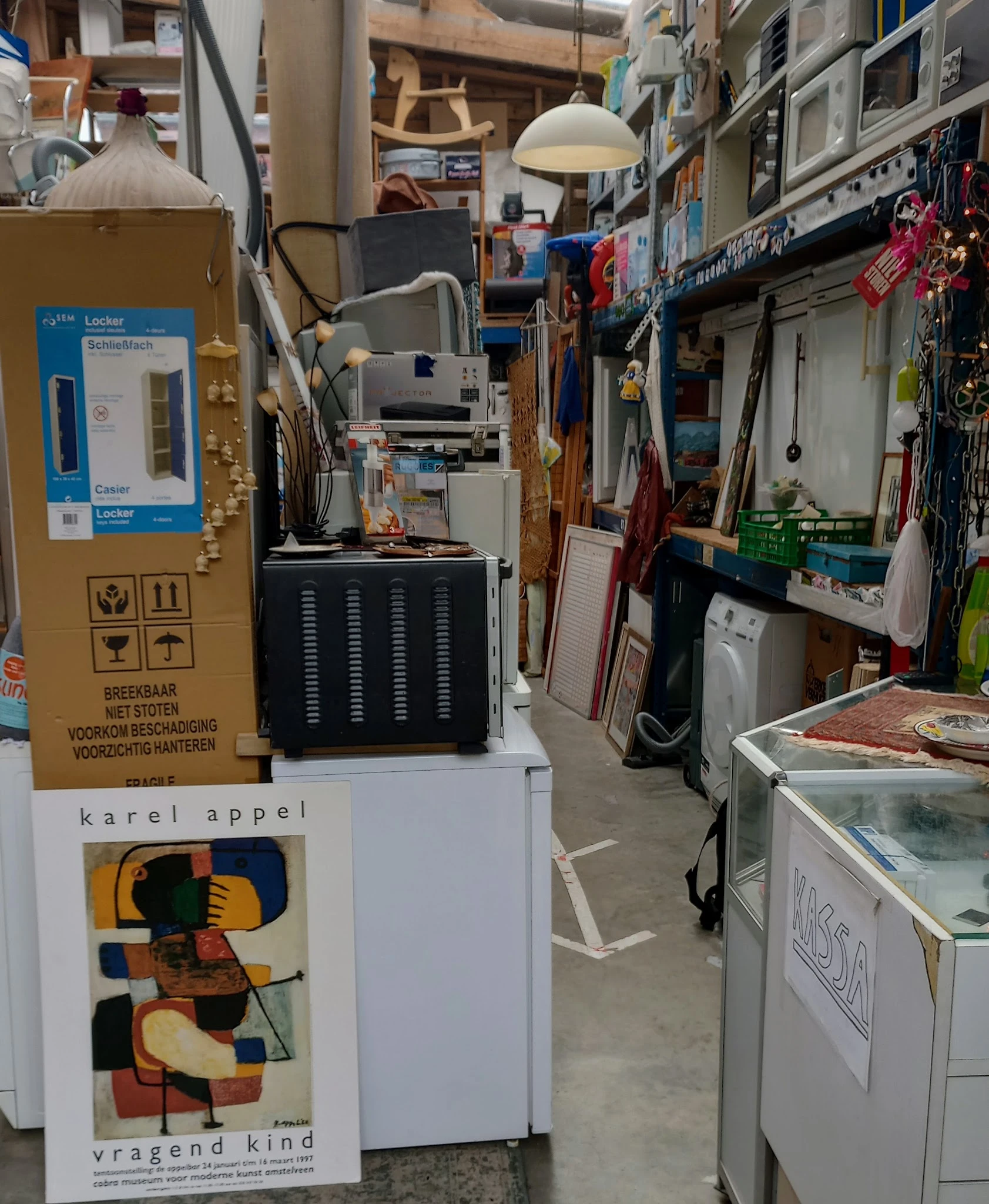 Binnenzijde kringloopwinkel met stellingen, diverse gebruikte artikelen en huishoudapparatuur