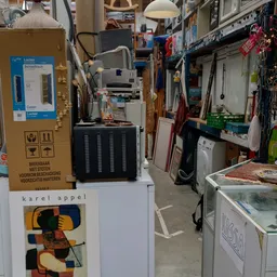 Binnenzijde kringloopwinkel met stellingen, diverse gebruikte artikelen en huishoudapparatuur