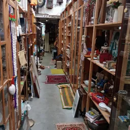 Lange gangpad in kringloopwinkel met houten kasten aan beide zijden, spullen op planken en kleine tapijten op de grond