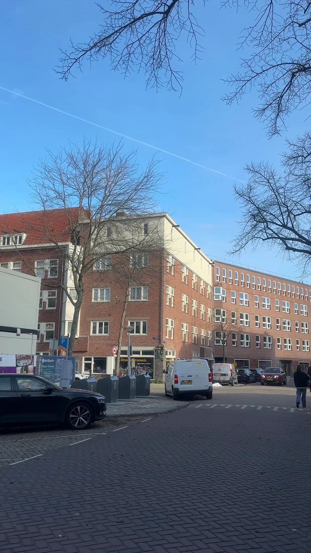 Straatgevel van rode baksteengebouwen met winkelpui beneden en parkeerplaats ervoor