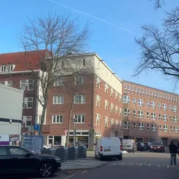 Straatgevel van rode baksteengebouwen met winkelpui beneden en parkeerplaats ervoor