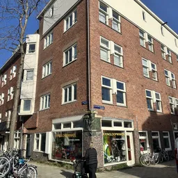 Bakstenen gevel van een kringloopwinkel met etalages op de begane grond en ramen op de bovenverdiepingen