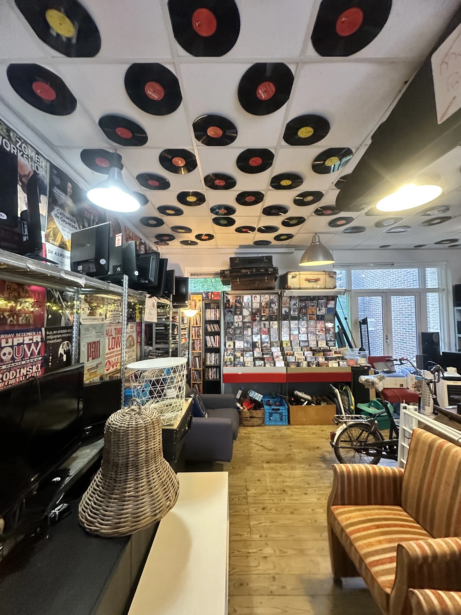 Winkelbinnenruimte met plafondversiering van vinyl records, displays met boeken en media, en diverse tweedehandsartikelen
