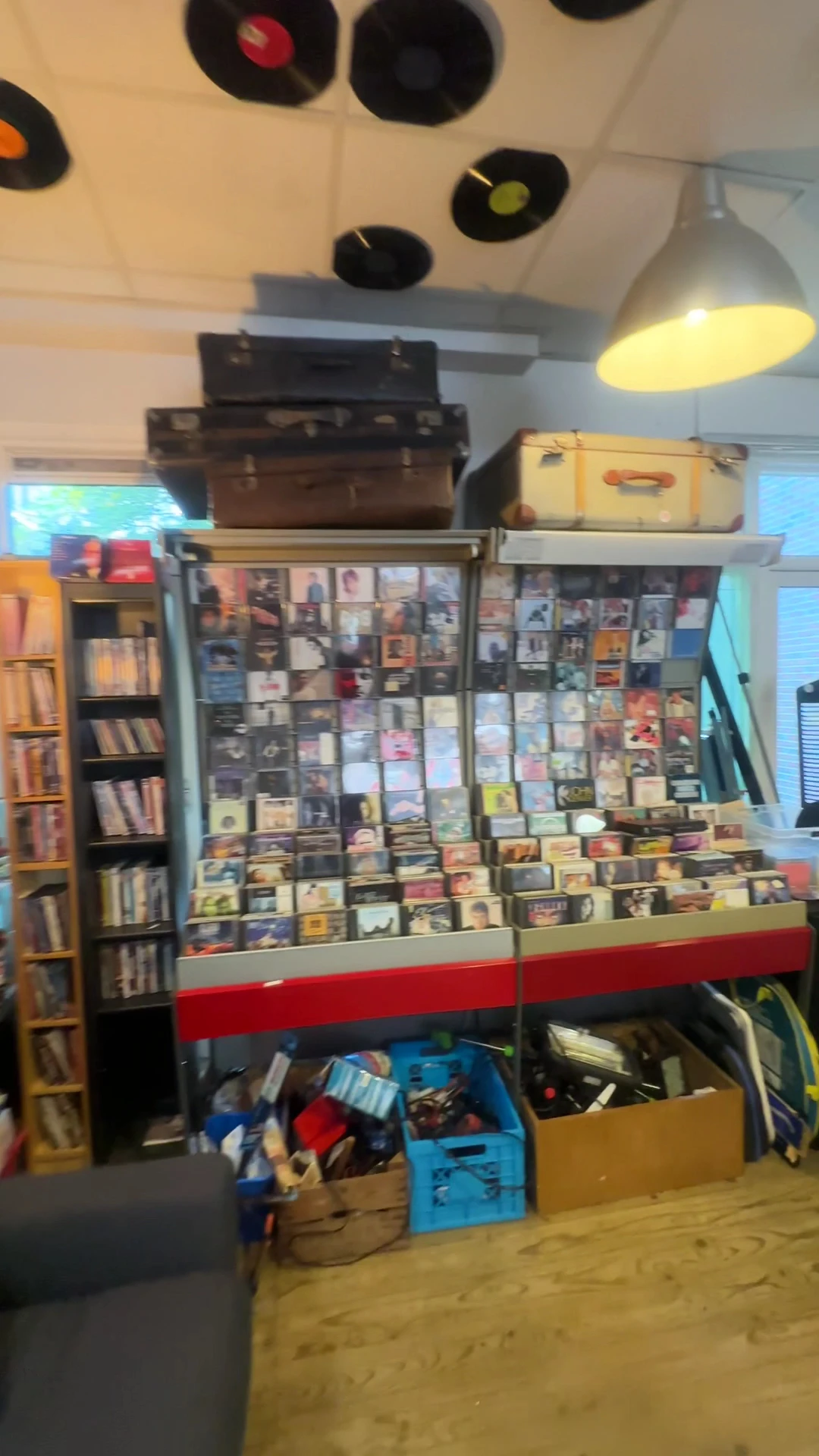 Uitgestalde cd's en dvd's in glazen vitrine met houten kisten erboven in kringloopwinkel