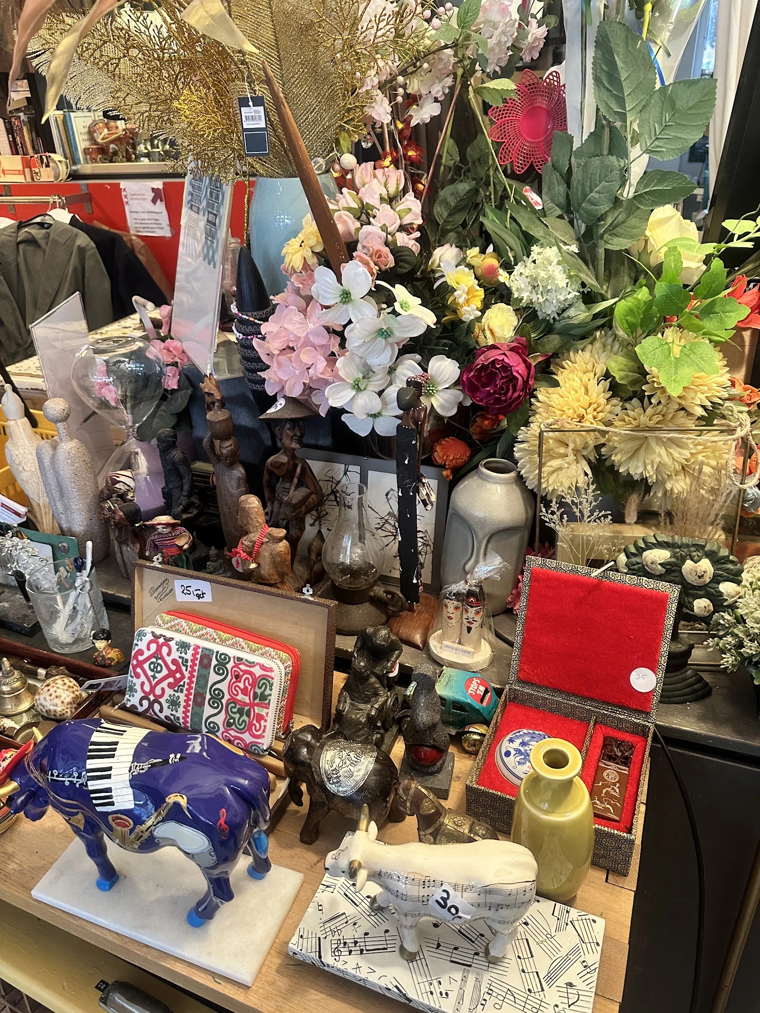 Uitgestalde tweedehands artikelen: kunstbloemen, decoratieve objecten, servies en huishoudelijke spullen op tafels