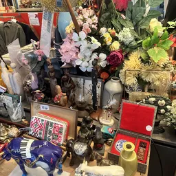 Uitgestalde tweedehands artikelen: kunstbloemen, decoratieve objecten, servies en huishoudelijke spullen op tafels
