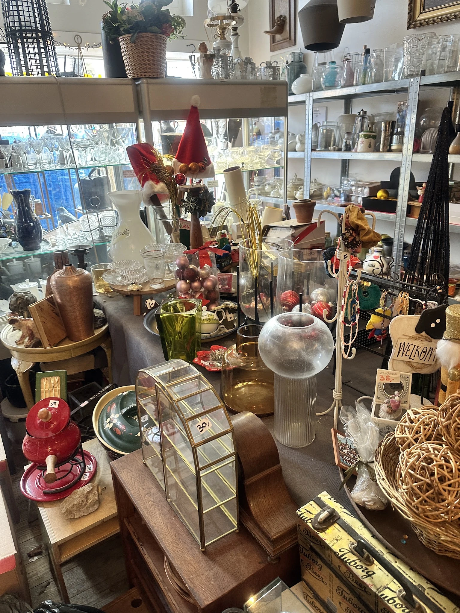 Uitgestalde decoratieve artikelen en huishoudspullen in kringloopwinkel, waaronder vazen, kandelaars, plantenstokken en diver