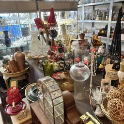 Uitgestalde decoratieve artikelen en huishoudspullen in kringloopwinkel, waaronder vazen, kandelaars, plantenstokken en diver