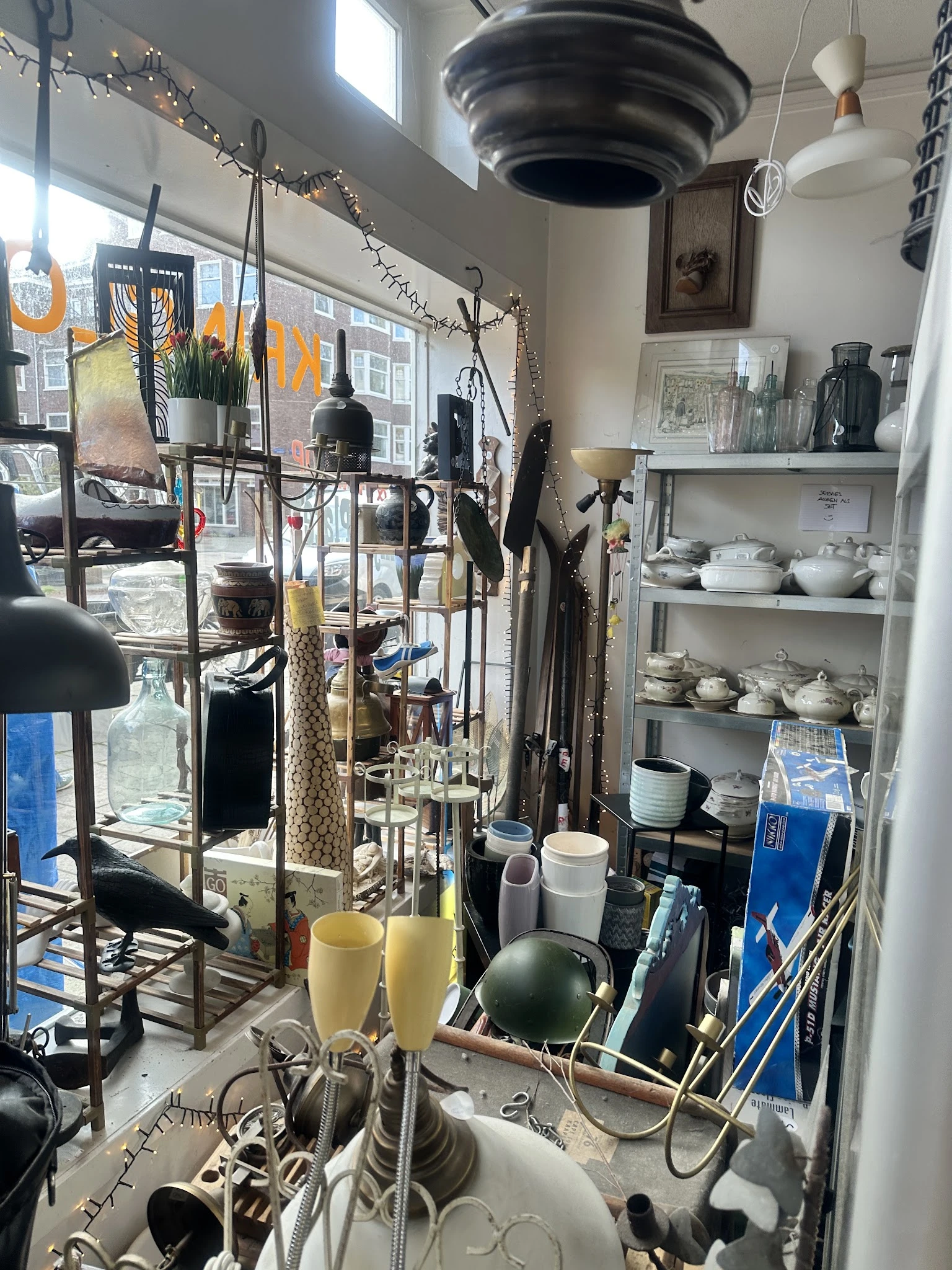 Stellingen en tafels met diverse huishoudelijke artikelen zoals servies, glazen, kandelaars en decoratieve voorwerpen